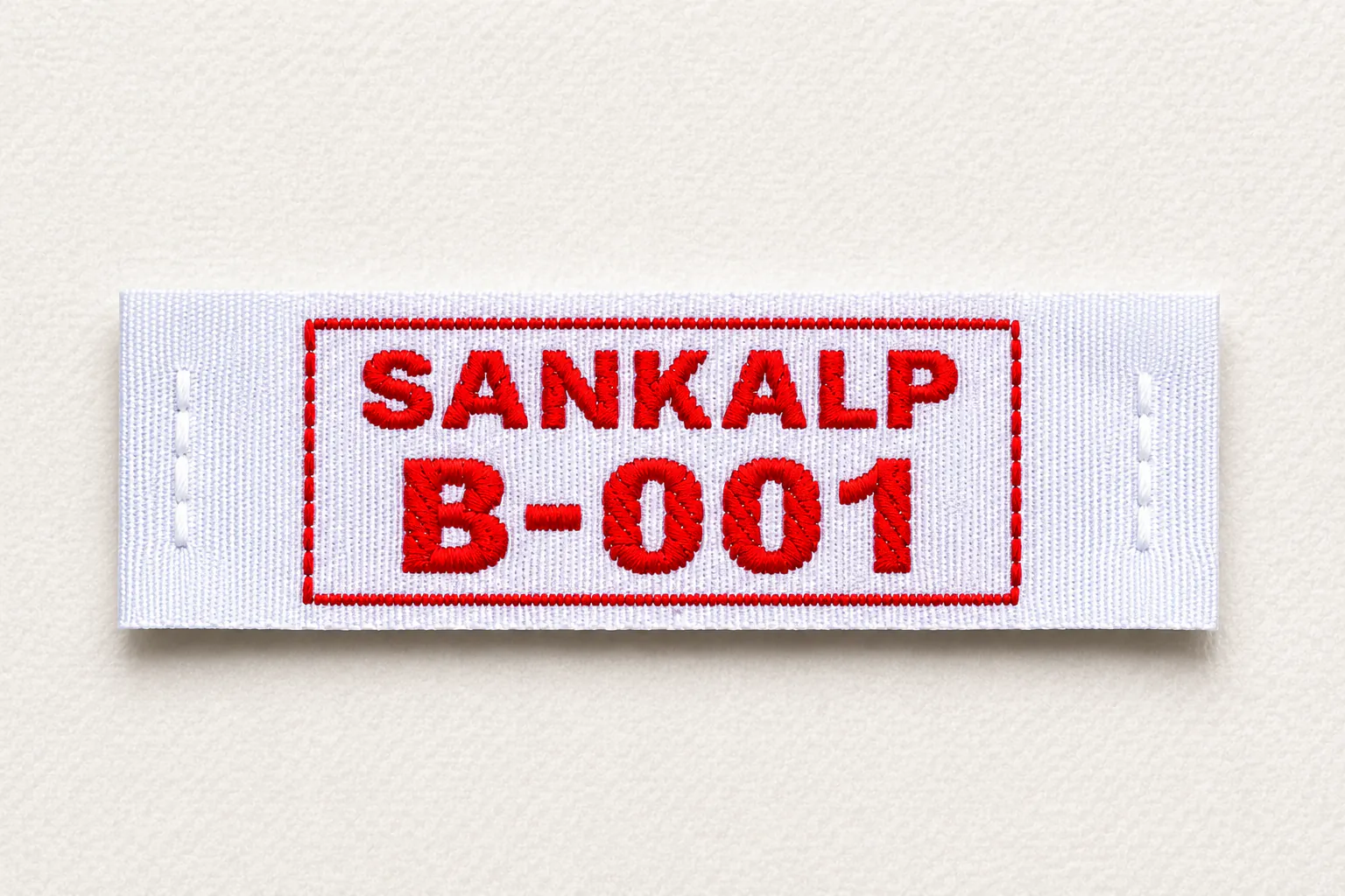 Sankalp B-001 white woven name and number label with red framed identifier — uniform identification woven label sample in red colourway