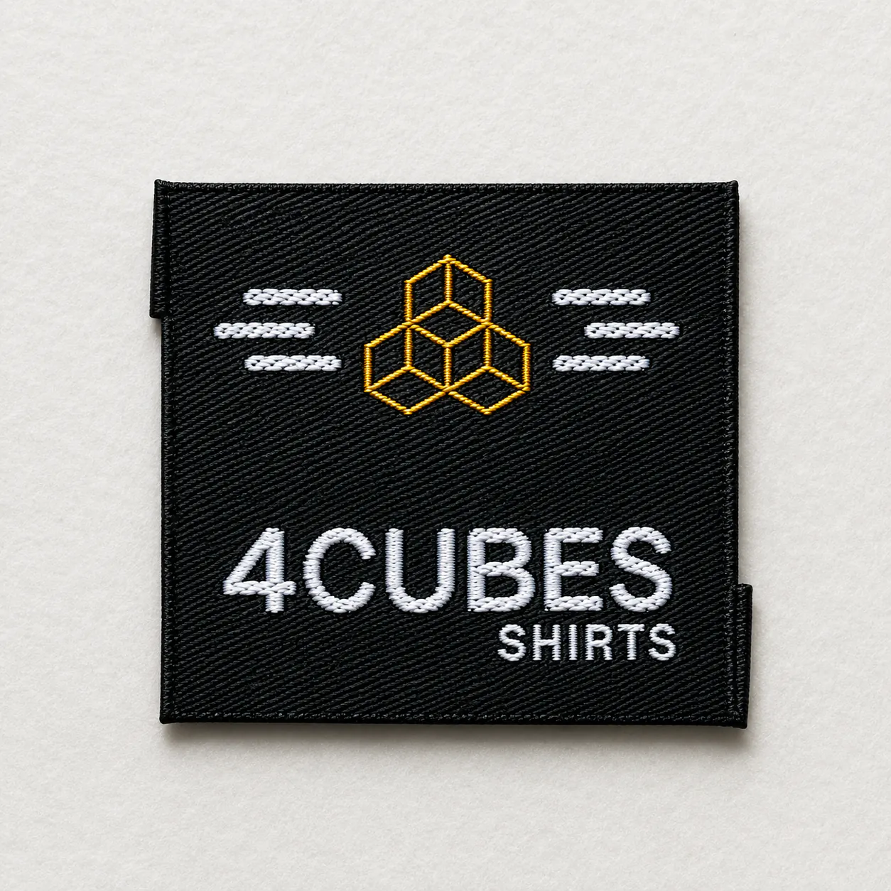 4Cubes Shirts black woven brand label with white wordmark, yellow geometric cubes logo and decorative stitched detailing — apparel brand woven label sample