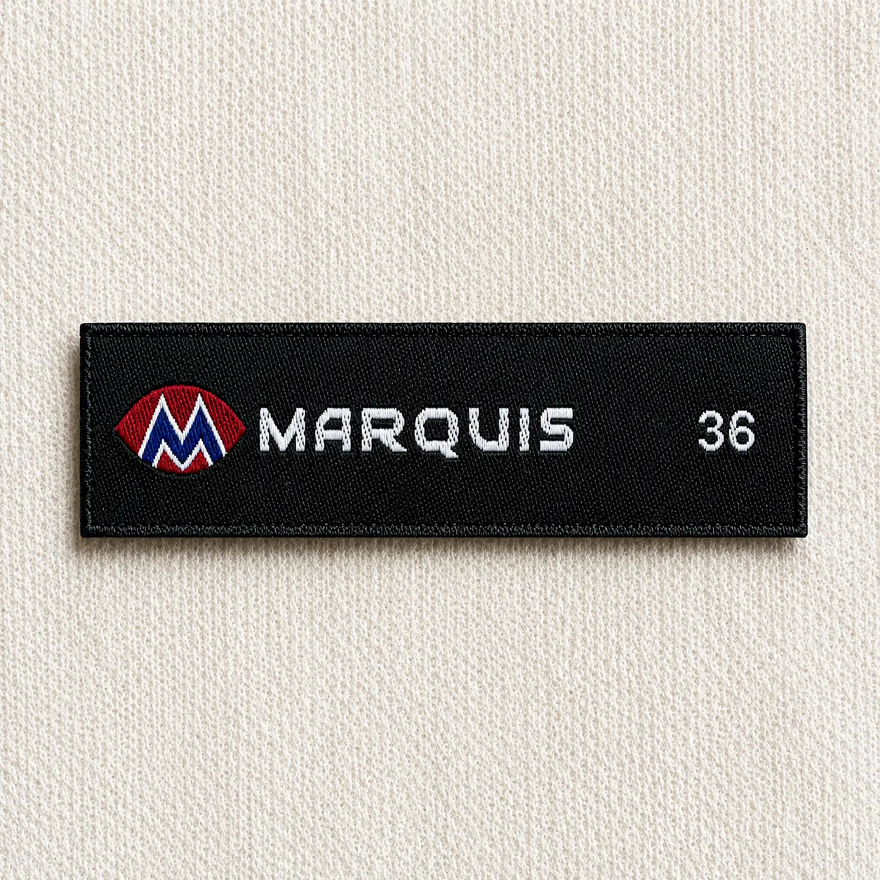 Marquis black woven brand label with red-and-white M logo, white wordmark and size 36 marker — menswear brand woven label sample
