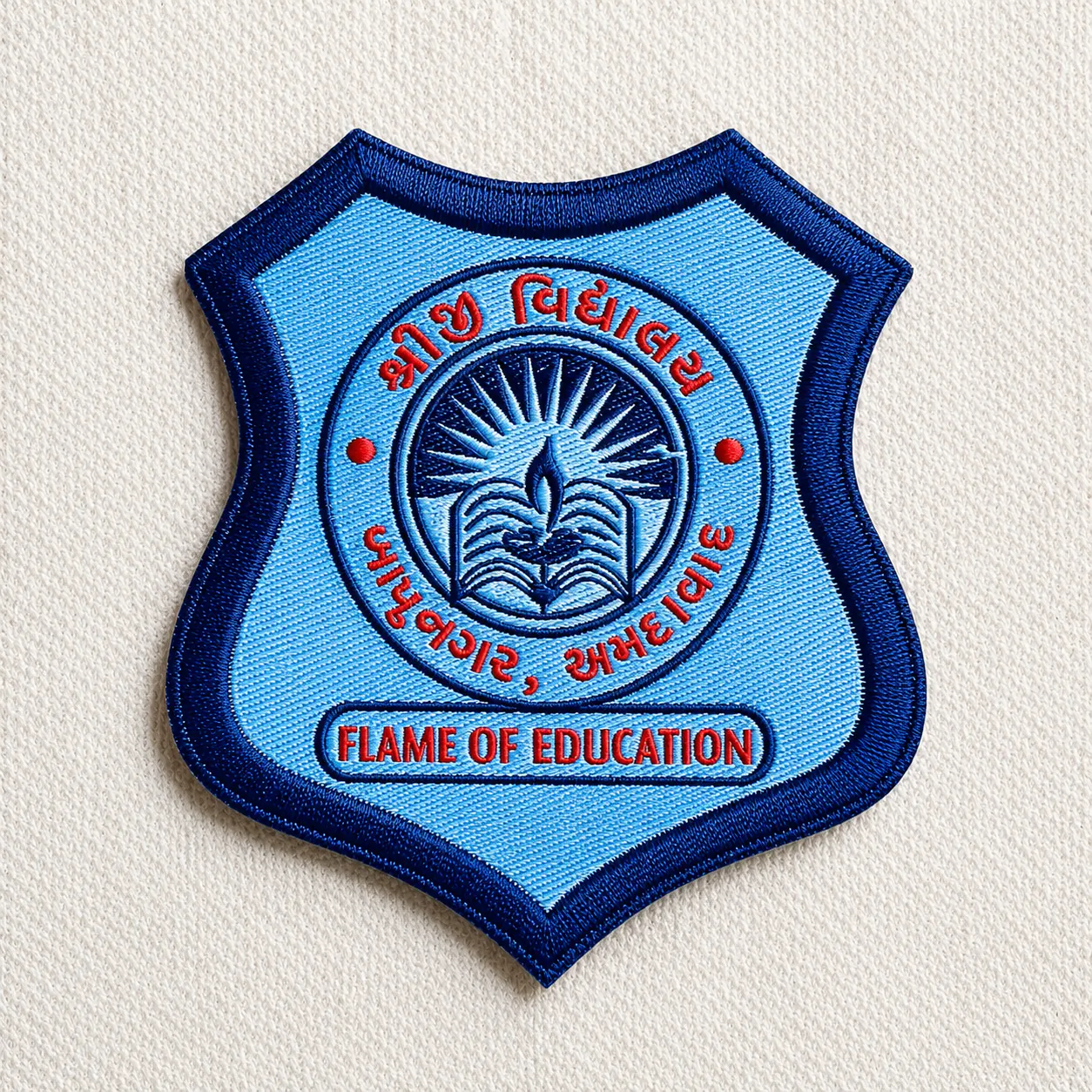 Shree Vidyalaya light-blue embroidered school crest patch with sun, lamp and open-book emblem and Flame of Education banner in Gujarati and English — school uniform embroidered patch sample