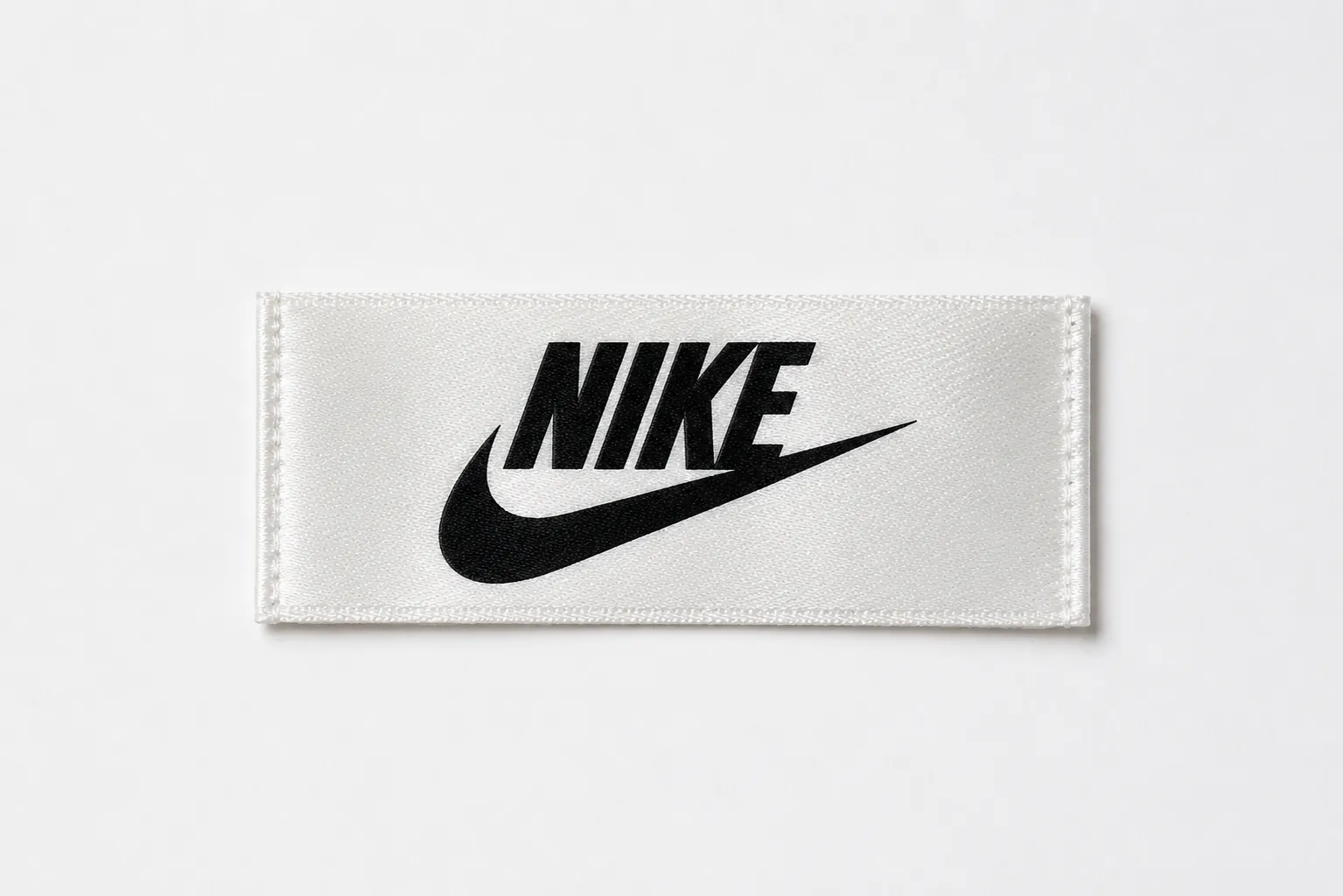 White satin printed brand label sample with bold black athletic swoosh-style logo and sans-serif wordmark — sportswear design reference, satin print finish