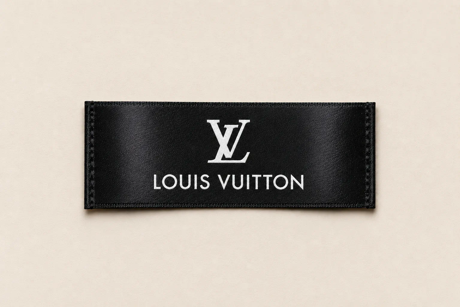 Black satin printed brand label sample with silver interlocking-letter monogram and serif wordmark — luxury fashion design reference, satin print finish