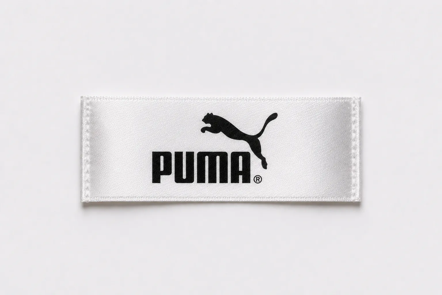 White satin printed brand label sample with bold black leaping-feline athletic logo and sans-serif wordmark — sportswear design reference, satin print finish